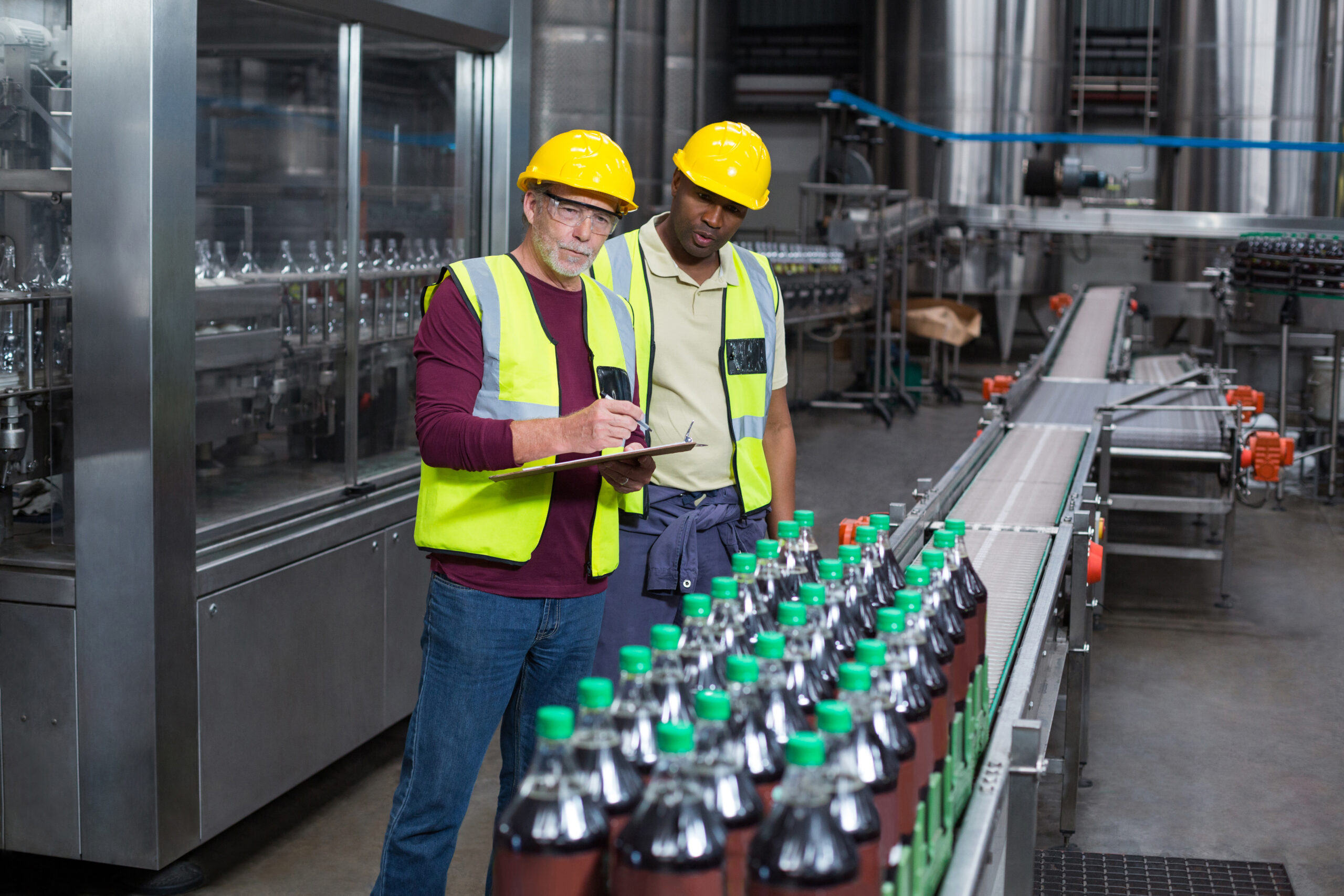 two factory workers monitoring cold drink bottles in the plant